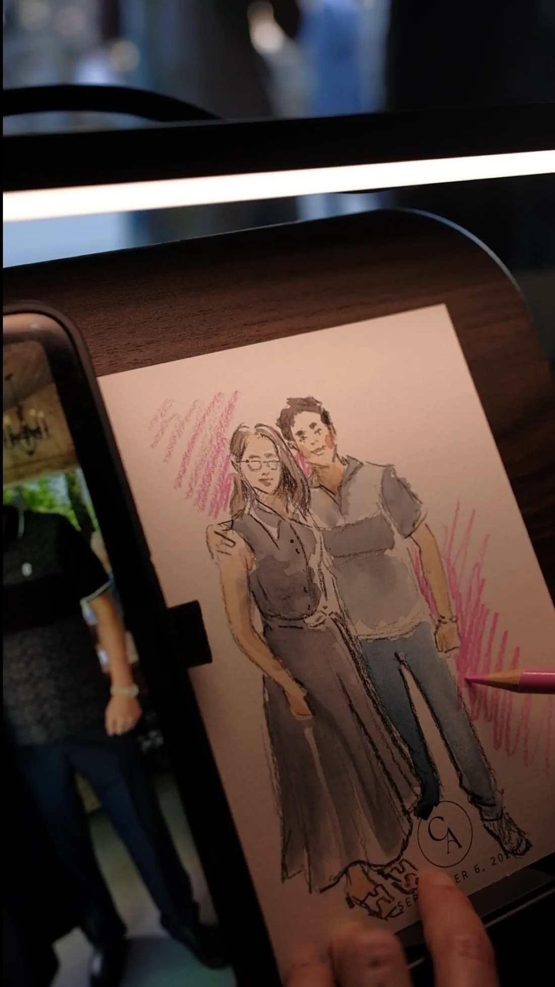 A completed illustrated portrait beside the reference photo of two guests.